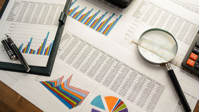 A magnifying glass examining various papers containing charts and analytics.